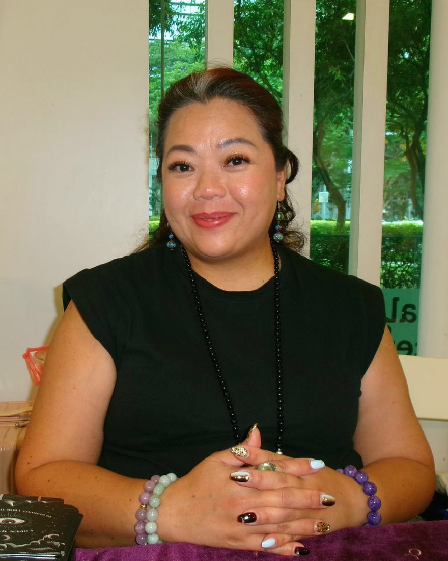 Perilla at her reading table, smiling, her hands folded on a purple cloth